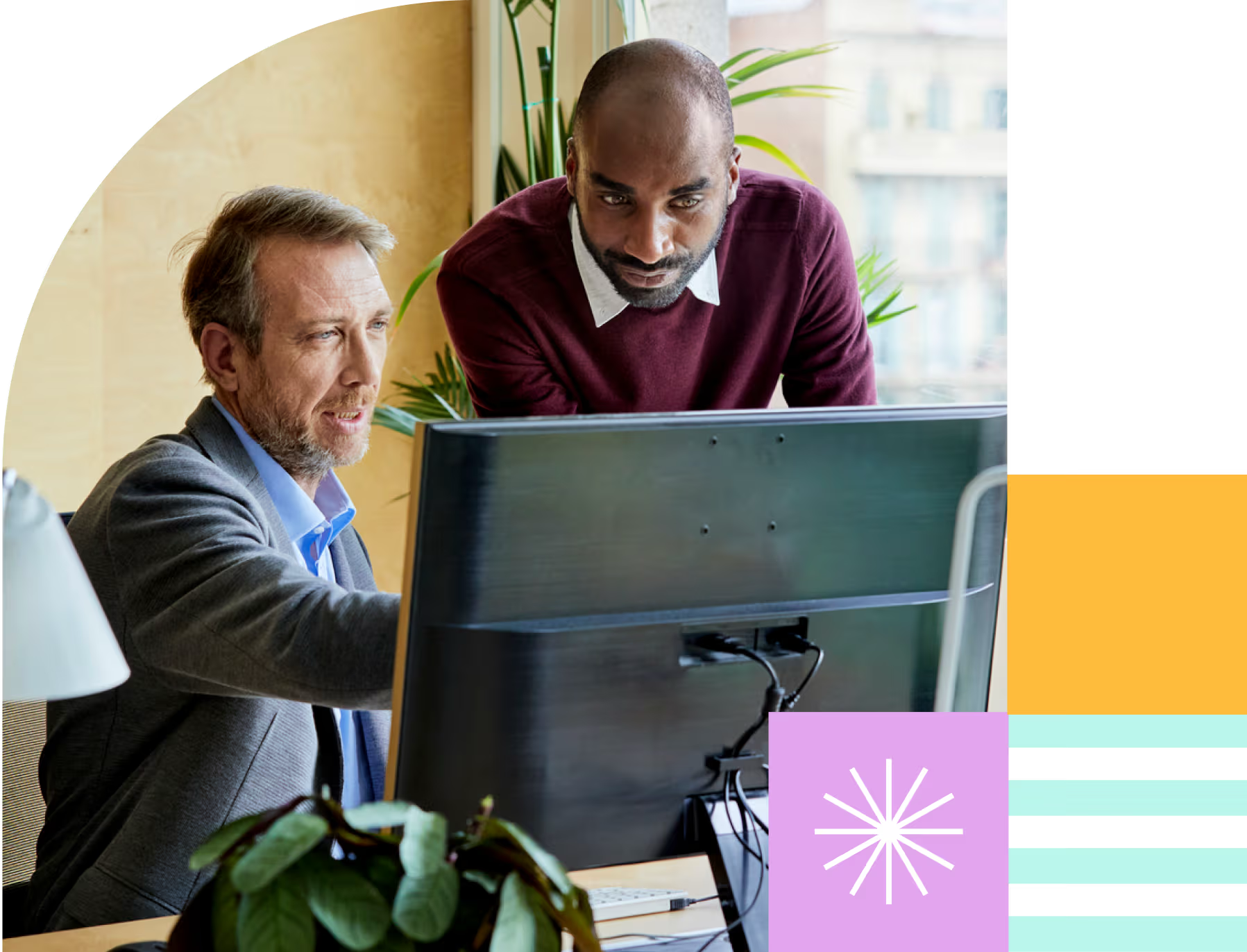 Two men collaborating in front of a computer monitor in a bright office space.